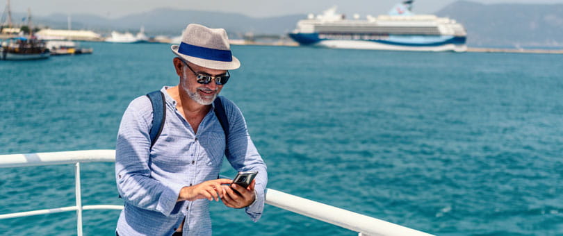 Person wearing a hat and sunglasses using a smartphone on a cruise ship deck