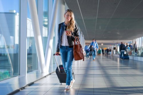 Woman walking in airport looking at mobile for blog post