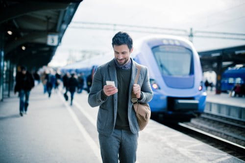 Man looking at mobile walking on train platform for blog post