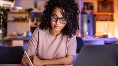 a women writing on a paper in front of a laptop.
