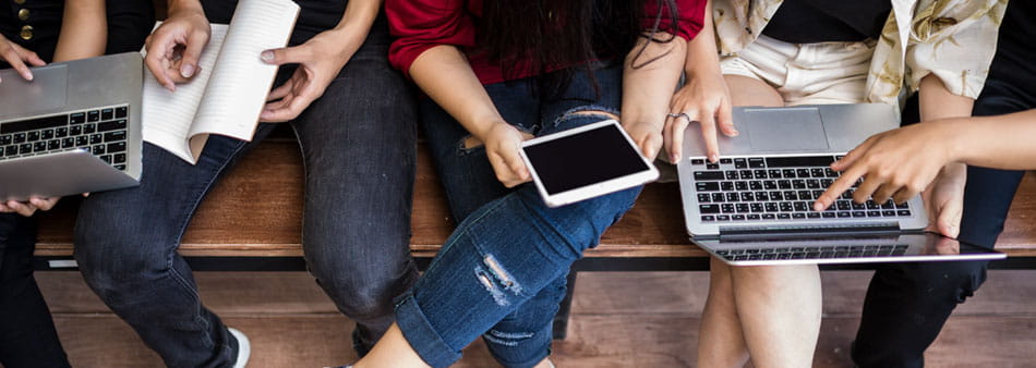legs of people sitting on a bench, with devices resting on their knees