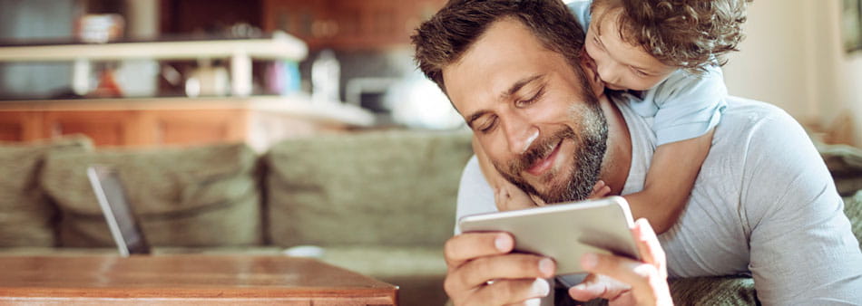 a child putting his arms around the neck of a man who is checking his smartphone